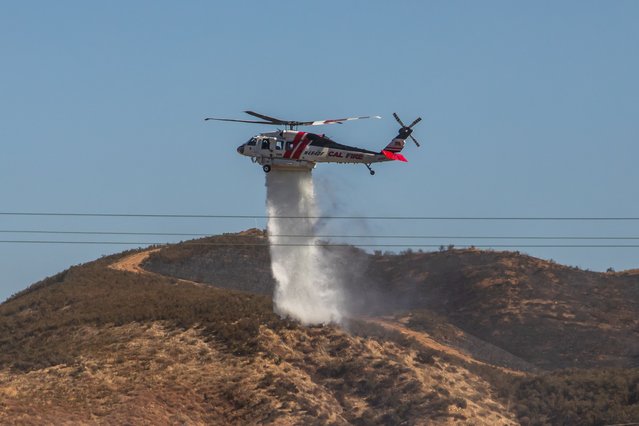 A CalFire firefighting helicopter drops water over the Hughes Fire in Castaic, a northwestern neighborhood of Los Angeles County, California, on January 23, 2025. (Photo by Apu Gomes/AFP Photo)