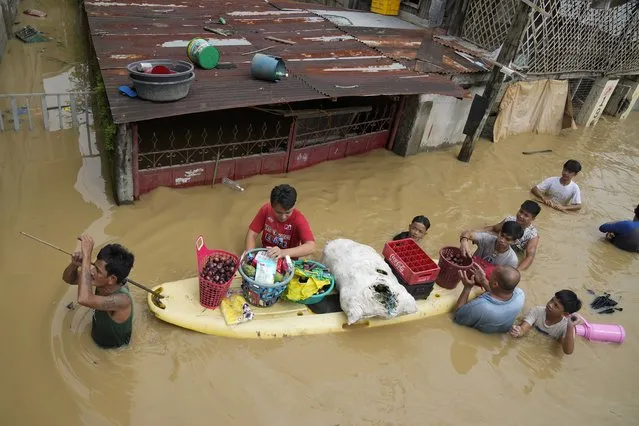 Residents give away onions and other foods along a flooded road due to Typhoon Noru in San Miguel town, Bulacan province, Philippines, Monday, September 26, 2022. Typhoon Noru blew out of the northern Philippines on Monday, leaving some people dead, causing floods and power outages and forcing officials to suspend classes and government work in the capital and outlying provinces. (Photo by Aaron Favila/AP Photo)
