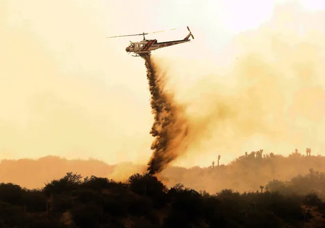 A helicopter makes a drop over a wildfire in West Cajon Valley, Calif., Wednesday, August 17, 2016. A day after the fire ignited in brush left tinder-dry by years of drought, the flames advanced despite the efforts of over 1,000 firefighters. (Photo by Alex Gallardo/AP Photo)
