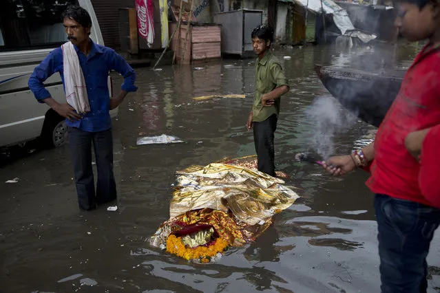 In this Friday, August 26, 2016 photo, a dead body lies in a flooded street before performing a Hindu funeral at the Harishchandra Ghat in Varanasi, India. As the mighty Ganges River overflowed its banks this past week following heavy monsoon rains, large parts of the Hindu holy town of Varanasi were submerged by floodwaters, keeping away thousands of devotees. Varanasi is a pilgrim town that Hindus visit to take a dip in the holy Ganges. Devout Hindus believe that if they are cremated on Varanasi’s ghats, or steps leading to the river, they earn immediate salvation and are freed from the cycle of birth and death. The ones most affected by the floods are those who have come to the town to cremate their loved ones. (Photo by Tsering Topgyal/AP Photo)