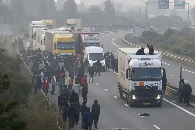 Migrants gather on the road as two board a lorry on the access road to reach the ferry terminal in Calais, France, October 3, 2015. (Photo by Pascal Rossignol/Reuters)