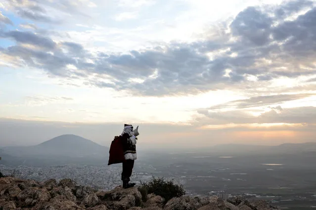 Issa Kassissieh, dressed as Santa Claus, waves and poses for members of the media as he stands on Mount Precipice in front of Mount Tabor close to Nazareth in northern Israel on December 12, 2022. (Photo by Nir Elias/Reuters)