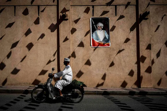 A man rides a motorcycle past a wall of the Nizwa fort bearing a portrait of the Omani Sultan before the first stage of the 2018 cycling Tour of Oman from Nizwa to the Sultan Qaboos University in Muscat on February 13, 2017. (Photo by Philippe Lopez/AFP Photo)