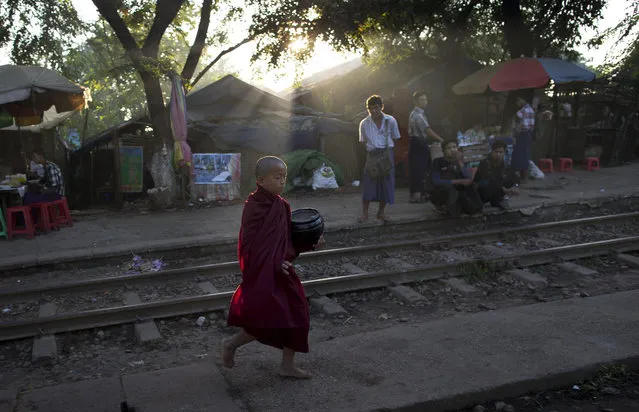 A novice Buddhist monk walks across a railway track collecting alms following a cleric's rule of no footwear nor use of umbrellas at a railway station in Yangon, Myanmar, Wednesday, November 26, 2014. (Photo by Gemunu Amarasinghe/AP Photo)