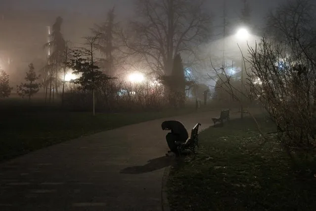 A man sits on a bench during a foggy night in a park in Belgrade, Serbia on January 22, 2023. (Photo by Marko Djurica/Reuters)