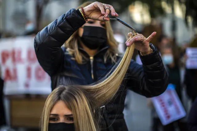A hairdresser cuts the hair of a woman as part of a protest of hairdressing and aesthetics sector in front of the Spanish parliament in Madrid, Spain, Tuesday, November 17, 2020. Although curfews and restrictions to travel between regions are pretty much widespread, Madrid has managed to bend the curve of contagion while keeping most commercial activity running while northeastern Catalonia has kept bars and restaurants closed for over a month now. (Photo by Manu Fernandez/AP Photo) 