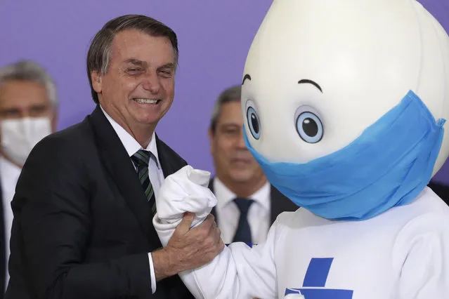 Brazilan President Jair Bolsonaro poses for photos with the mascot of his nation's vaccination campaign, named “Ze Gotinha”, or Joseph Droplet, during a ceremony to present the National Vaccination Plan Against COVID-19 at Planalto presidential palace in Brasilia, Brazil, Wednesday, December 16, 2020. (Photo by Eraldo Peres/AP Photo)