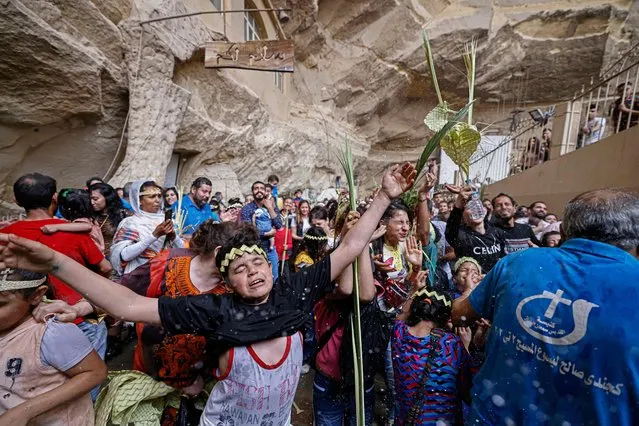 Egyptian Coptic Christians react as they get sprayed with holy water during Palm Sunday Mass at the Saint Simon Monastery, also known as the Cave Church, in Cairo's Mokattam mountain on April 9, 2023. (Photo by Khaled Desouki/AFP Photo)