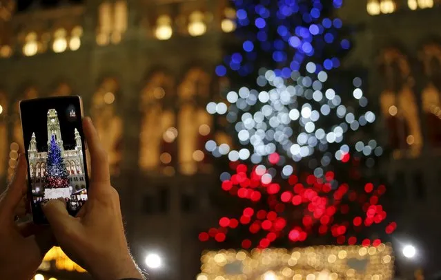 A tourist takes a picture of a Christmas tree lit in the blue, white and red colours of France's national flag in tribute to victims of last Friday's attacks in Paris, in front of the city hall in Vienna, Austria, November 19, 2015. (Photo by Leonhard Foeger/Reuters)
