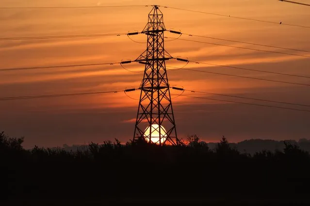 The sun rises behind an electricity transmission tower in the U.K. on March 14, 2022. (Photo by Chris Ratcliffe/Bloomberg)
