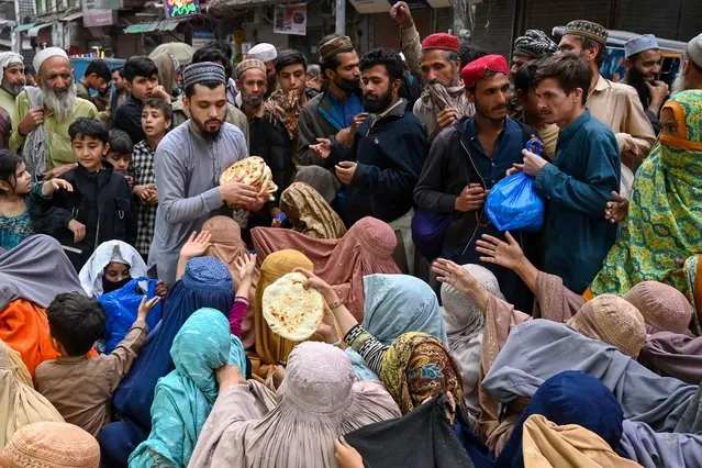Burqa-clad women wait for free bread at a distribution point in Peshawar on April 3, 2023. Poor Pakistanis are feeling the brunt of the economic turmoil, and at least 20 people have been killed since the start of the Muslim fasting month of Ramadan in crowd crushes at food distribution centres. (Photo by Abdul Majeed/AFP Photo)