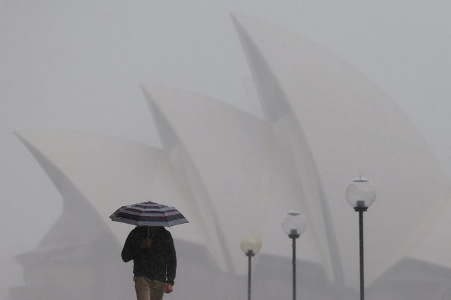 A person carrying an umbrella shelters from the rain as they walk past the Sydney Opera House in Sydney, Australia, on August 21, 2025. (Photo by Hollie Adams/Reuters)