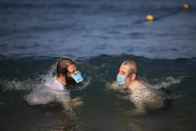 Ultra-orthodox Jewish men wearing protective face masks swim in the Mediterranean Sea, on a beach segregated for males three days a week, in Tel Aviv, Israel, Wednesday, July 8, 2020. In an effort to quell the rapid spread of the coronavirus, Israel has re-imposed a series of restrictions on the public. This week, the Israeli government limited gatherings and ordered reception halls, restaurants, bars, theaters, fitness centers and pools be shut down again. (Photo by Oded Balilty/AP Photo)