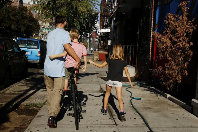 A family walks a bicycle down a sidewalk on an unseasonably warm day in the Brooklyn borough of New York, U.S., October 18, 2016. (Photo by Lucas Jackson/Reuters)