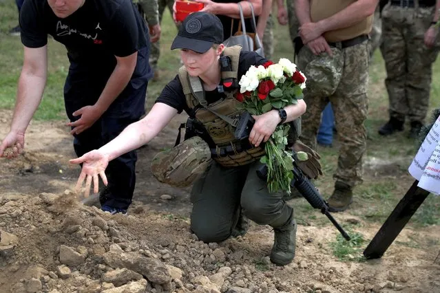 A Ukrainian servicewoman throws sand into a grave of Evgeny Khrapko, a combat medic and instructor of tactical medicine who was killed in a mission, amid Russia's attack on Ukraine, during his farewell ceremony in Kharkiv, Ukraine on June 14, 2022. (Photo by Ivan Alvarado/Reuters)