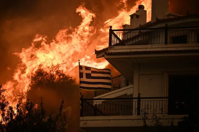 A Greek flag flutters in the wind during a wildfire in Chasia in the outskirts of Athens on August 22, 2023. Greece's fire brigade on August 22, 2023 ordered the evacuation of a district on Athens' northwestern flank as firefighters battled a steadily growing wave of wildfires around the country, the second in a month. Tens of thousands of people have been urged to leave the district of Ano Liosia, while at the neighbouring community of Fyli an AFP journalist saw homes on fire. (Photo by Angelos Tzortzinis/AFP Photo)