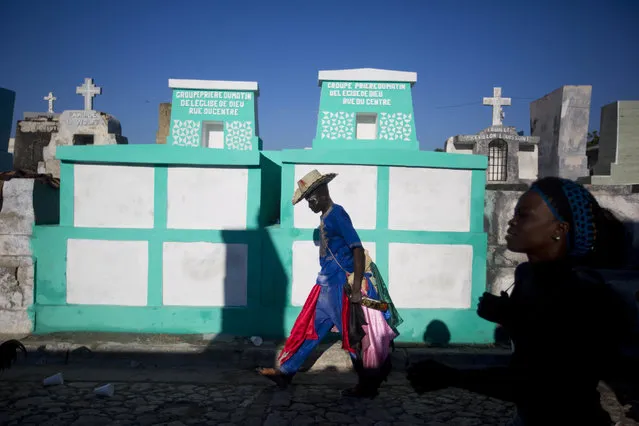 In this Novemer 1, 2018 photo, a voodoo believer walks to Baron Samedi's tomb during the annual Voodoo festival Fete Gede at Cite Soleil Cemetery in Port-au-Prince, Haiti. The most respected along the Fete Gede is Baron Samedi, a lewd representation of life and death, who runs the gate of the Guiné (a kind of Heaven) wearing a black suit and top hat while drinking alcohol, smoking tobacco and following young ladies in a provocative manner. (Photo by Dieu Nalio Chery/AP Photo)