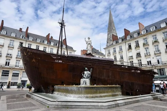 Passers-by stand next to the artwork “Le Naufrage de Neptune” (Neptune's Sinking) of French artist Ugo Schiavi, displayed behind a fountain on July 2, 2021 in Nantes, western France, as part of the “Voyage a Nantes” (VAN) art festival which runs from July 03 to September 12, 2021. (Photo by Sebastien Salom-Gomis/AFP Photo)