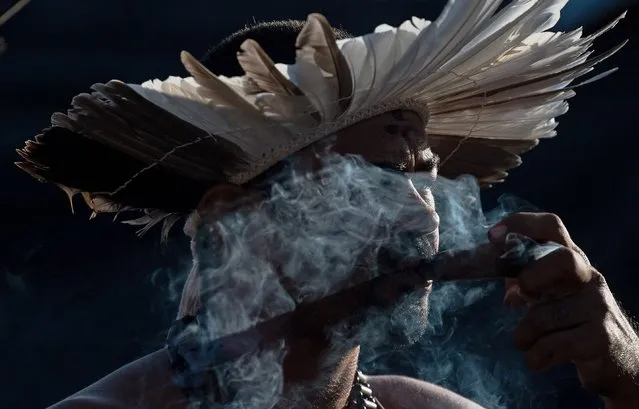 A man from the Kambiwa tribe of Pernambuco smokes a pipe during a traditional ritual at an indigenous protest camp on the second day of the Terra Livre Indigenous Camp in Brasilia on April 5, 2022. The 10-day annual protest, which is held by indigenous people from tribes that arrive from all over Brazil, calls for greater protection of their land and rights. (Photo by Carl de Souza/AFP Photo)