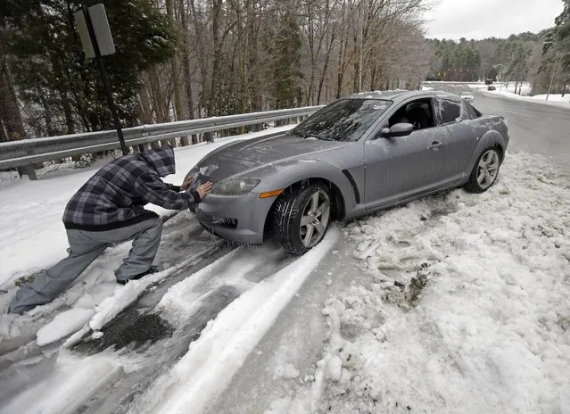 Passerby Leo Cruz helps push a car from the frozen roadside in Chapel Hill, N.C., Thursday, February 13, 2014. The owner abandoned the car overnight during the storm. The National Weather Service issued a winter storm warning lasting into Thursday covering 95 of the state's 100 counties. (Photo by Gerry Broome/AP Photo)