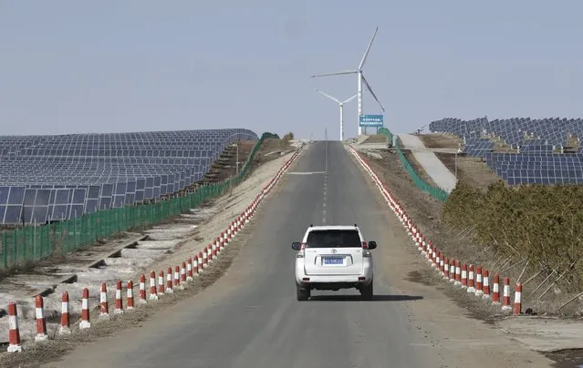 A vehicle drives past the solar panels near wind turbines at a wind and solar energy storage and transmission power station of State Grid Corporation of China, in Zhangjiakou of Hebei province, China, March 18, 2016. (Photo by Jason Lee/Reuters)