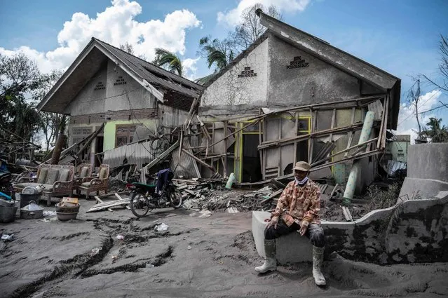 A man sits outside damaged buildings in the village of Curah Kobokan in Lumajang on December 9, 2021, after the eruption of Mount Semeru volcano on December 4 killed at least 39 people. (Photo by Juni Kriswanto/AFP Photo)