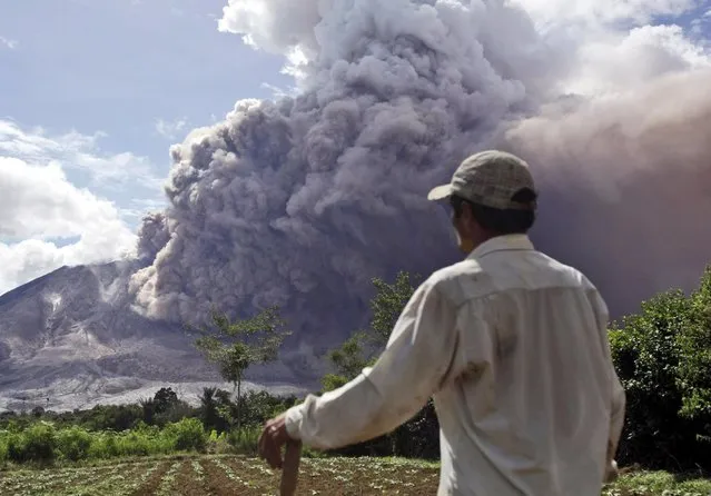 A farmer watches as Mount Sinabung releases pyroclastic flows in Tiga Pancur, North Sumatra, Indonesia, Saturday, June 13, 2015. The volcano, which was put on it highest alert level last week, has sporadically erupted since 2010 after being dormant for 400 years. (AP Photo/Binsar Bakkara)