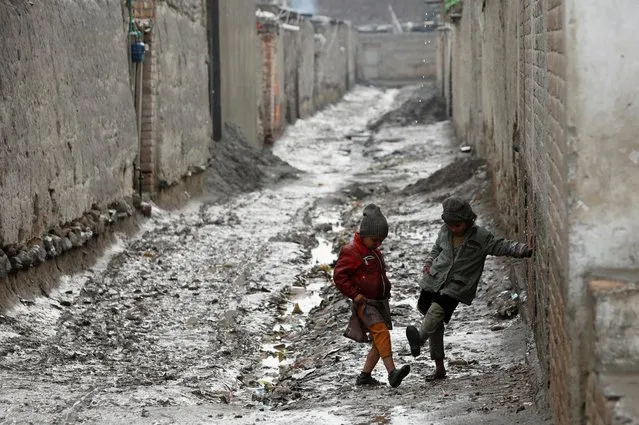 Children play along a muddy street after rain in Peshawar, Pakistan on January 5, 2022. (Photo by Fayaz Aziz/Reuters)
