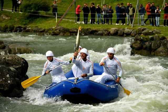 French slalom canoeist Patrice Estanguet (C) holds the Olympic flame while heading down the whitewater venue as part of the Olympic torch relays, in Pau, southwestern France, on May 20, 2024, ahead of the Paris 2024 Olympic and Paralympic Games. (Photo by Gaizka Iroz/AFP Photo)