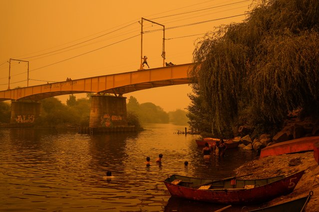 People wade in the Renaico river under a smoked-filled sky caused by wildfires, in Renaico, Chile, Saturday, February 4, 2023. Wildfires are spreading in southern and central Chile, triggering evacuations and the declaration of a state of emergency in some regions. (Photo by Matias Delacroix/AP Photo)