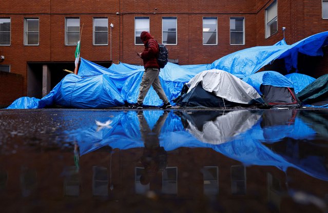 An asylum seeker walks past tents beside the International Protection Office (IPO), where hundreds of migrants in search of accommodation have been sleeping on the streets for several months with more arriving every day, Dublin, Ireland, April 30, 2024. (Photo by Clodagh Kilcoyne/Reuters)