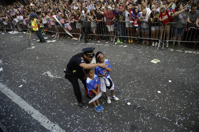 A police officer with two U.S. women's soccer team fans points as the floats with players makes its way up Broadway's Canyon of Heroes during the ticker tape parade to celebrate the World Cup victory, Friday, July 10, 2015, in New York. (Photo by Mary Altaffer/AP Photo)