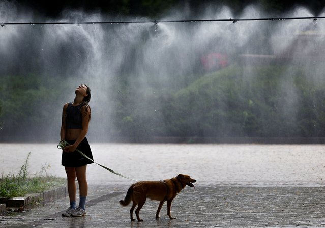 A woman with a dog cools herself under a water sprinkler on an extremely hot summer day, amid Russia's attack on Ukraine, in a park in central Kyiv, Ukraine on July 16, 2024. (Photo by Valentyn Ogirenko/Reuters)