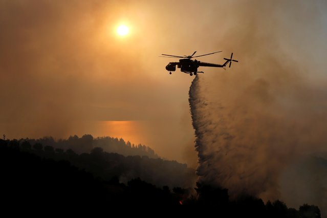 A firefighting helicopter makes a water drop as a wildfire burns near the village of Ziria, near Patras, Greece, August 1, 2021. (Photo by Costas Baltas/Reuters)