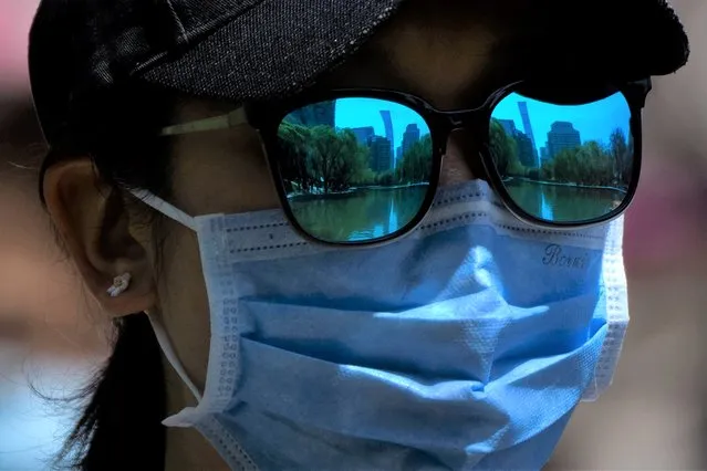 The skyline of Beijing is reflecting in the sunglasses of a woman wearing a face mask as she walks at a public park in Beijing, Thursday, April 14, 2022. (Photo by Mark Schiefelbein/AP Photo)