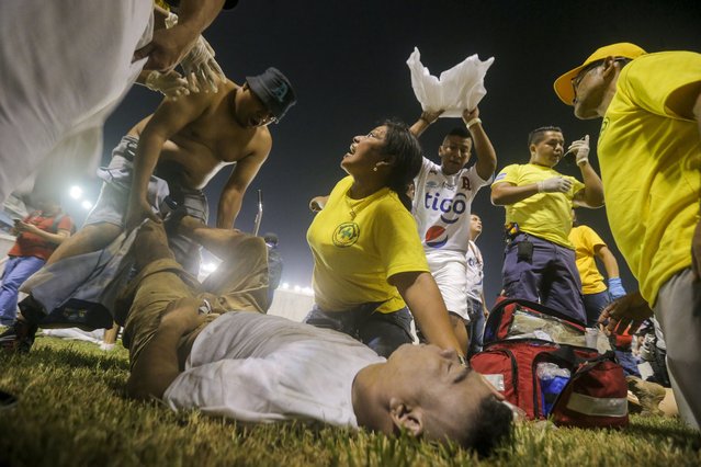 Rescuers attend an injured fan lying on the field of the Cuscatlan stadium in San Salvador, El Salvador, Saturday, May 20, 2023. At least nine people were killed and dozens more injured when stampeding fans pushed through one of the access gates at a quarterfinal Salvadoran league soccer match between Alianza and FAS. (Photo by Milton Flores/AP Photo)