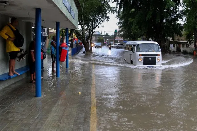 A woman stands on a bus stop bench as a driver of a Volkswagen van navigates a flooded street in Recife, state of Pernambuco, Brazil, Saturday, May 28, 2022. Landslides caused by heavy rains killed at least 29 people on Saturday. Authorities say that in Alagoas, another state in the region, two people died when they were swept away in river flooding on Friday. (Photo by Marlon Costa/Futura Press via AP Photo)