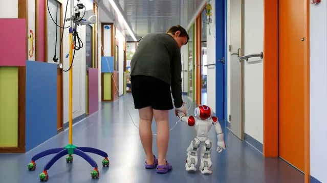 Belgian Ian Frejean, 11, walks with “Zora” the robot, a humanoid robot designed to entertain patients and to support care providers, at AZ Damiaan hospital in Ostend, Belgium June 16, 2016. (Photo by Francois Lenoir/Reuters)
