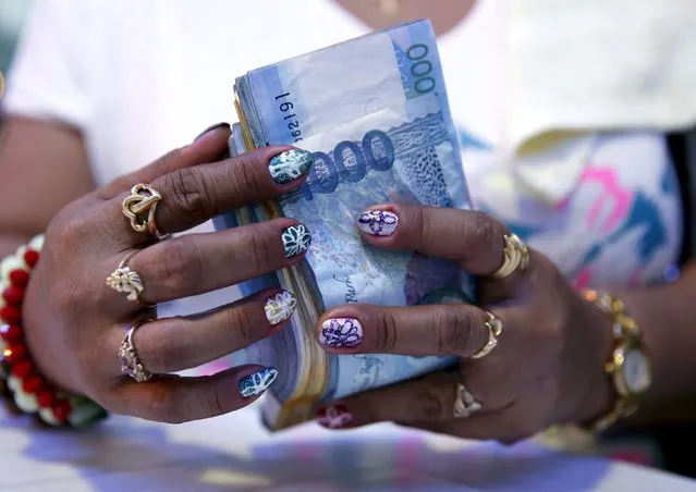 A casino financier wearing rings and with painted fingernails, counts money she collected from a gambler only moments before, in Angeles city, north of Manila, Philippines, in this May 25, 2015 file photo. (Photo by Erik De Castro/Reuters)