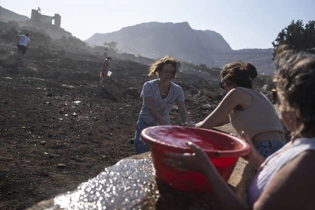 German tourists together with local residents try to extinguish a fire, near the seaside resort of Lindos, on the Aegean Sea island of Rhodes, southeastern Greece, on Monday, July 24, 2023. A weeklong wildfire on the Greek resort island of Rhodes tore past defenses Monday, forcing more evacuations, as three major fires raged elsewhere in the country fueled by strong winds and successive heat waves that left scrubland and forests tinder-dry. (Photo by Petros Giannakouris/AP Photo)