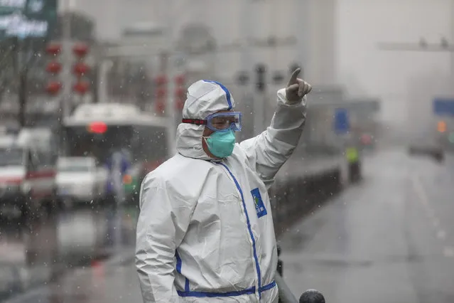A worker wearing a protective suit gestures to a driver outside a tumor hospital newly designated to treat COVID-19 patients in Wuhan in central China's Hubei Province, Saturday, February 15, 2020. The virus is thought to have infected more than 67,000 people globally and has killed at least 1,526 people, the vast majority in China, as the Chinese government announced new anti-disease measures while businesses reopen following sweeping controls that have idled much of the economy. (Photo by Chinatopix via AP Photo)