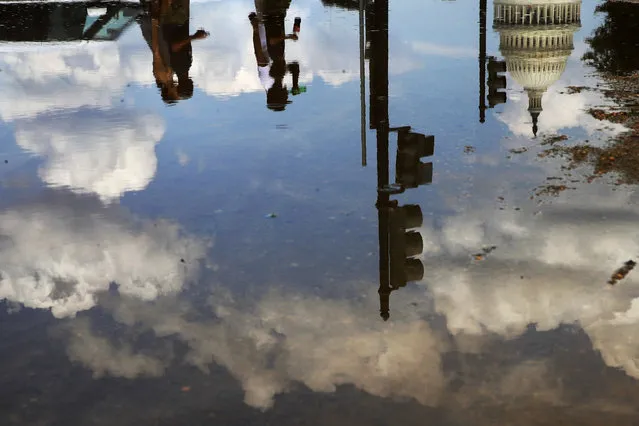 Tourists and the Capitol dome are reflected in a puddle left from sprinklers watering the lawn of the National Mall during turf restoration efforts, Thursday, August 10, 2017, in Washington. (Photo by Jacquelyn Martin/AP Photo)