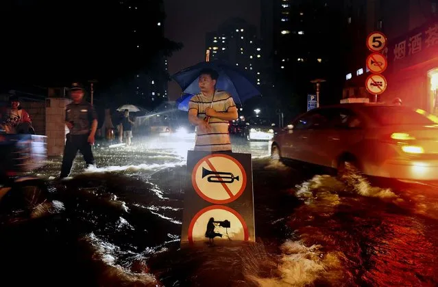 A man uses a signboard to signal motorists driving through flooded streets following the heaviest rains to hit Beijing in six decades on July 21, 2012. (Photo by Associated Press)