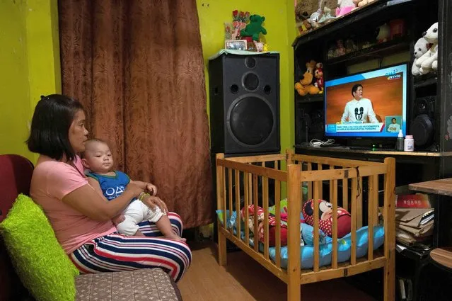 A woman carries her son as she watches Philippine President Ferdinand Marcos Jr's first State of the Nation Address on television at their home in Quezon City, Metro Manila, Philippines on July 25, 2022. (Photo by Lisa Marie David/Reuters)
