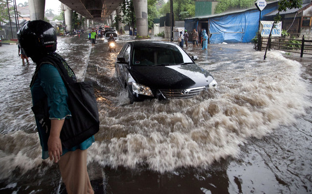 A car drives through a flooded road in Jakarta, Indonesia, Monday, August 11, 2014. The unseasonal rains flooded many areas of South Jakarta in the late afternoon causing much traffic congestion as commuters attempted to make their way home. (Photo by Mark Baker/AP Photo)