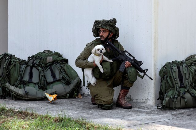 An Israeli soldier holds a rescued dog as he takes position near a bomb shelter in Kibbutz Kfar Aza, in southern Israel on October 10, 2023. (Photo by Ronen Zvulun/Reuters)