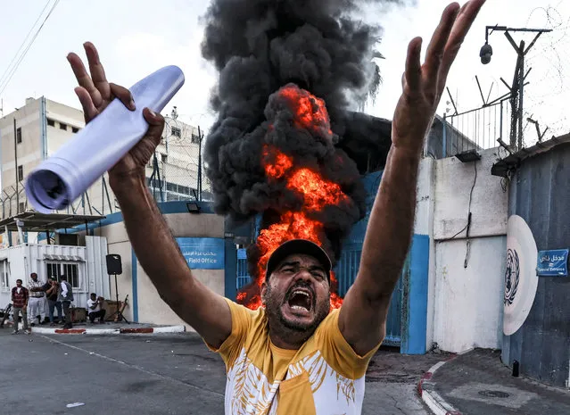 A Palestinian protester chants slogans by tires set aflame by the Gaza City headquarters of the United Nations Relief and Works Agency for Palestine Refugees (UNRWA) on September 19, 2022, during a demonstration demanding that their homes which were destroyed in the 2014 conflict with Israel be rebuilt. (Photo by Mahmud Hams/AFP Photo)