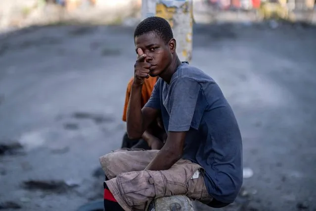 A young man gestures while sitting on a concrete road divider on a quiet street usually packed with people and heavy traffic in Port-au-Prince, Haiti on October 12, 2022. (Photo by Ricardo Arduengo/Reuters)