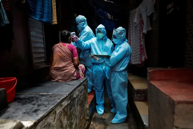 Healthcare workers wearing personal protective equipment (PPE) check the temperature of a resident at a slum during a check-up camp for the coronavirus disease (COVID-19) in Mumbai, India June 14, 2020. (Photo by Francis Mascarenhas/Reuters)