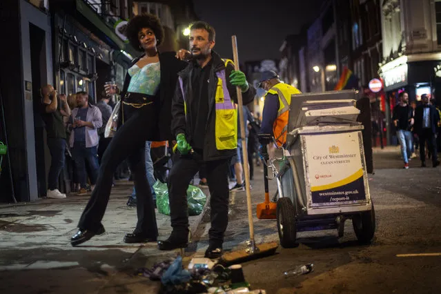 A woman poses with a street cleaner in Soho as late-night drinkers continue into the early hours of Sunday morning as coronavirus lockdown restrictions are eased across England, Sunday July 5, 2020. (Photo by Victoria Jones/PA Wire via AP Photo)